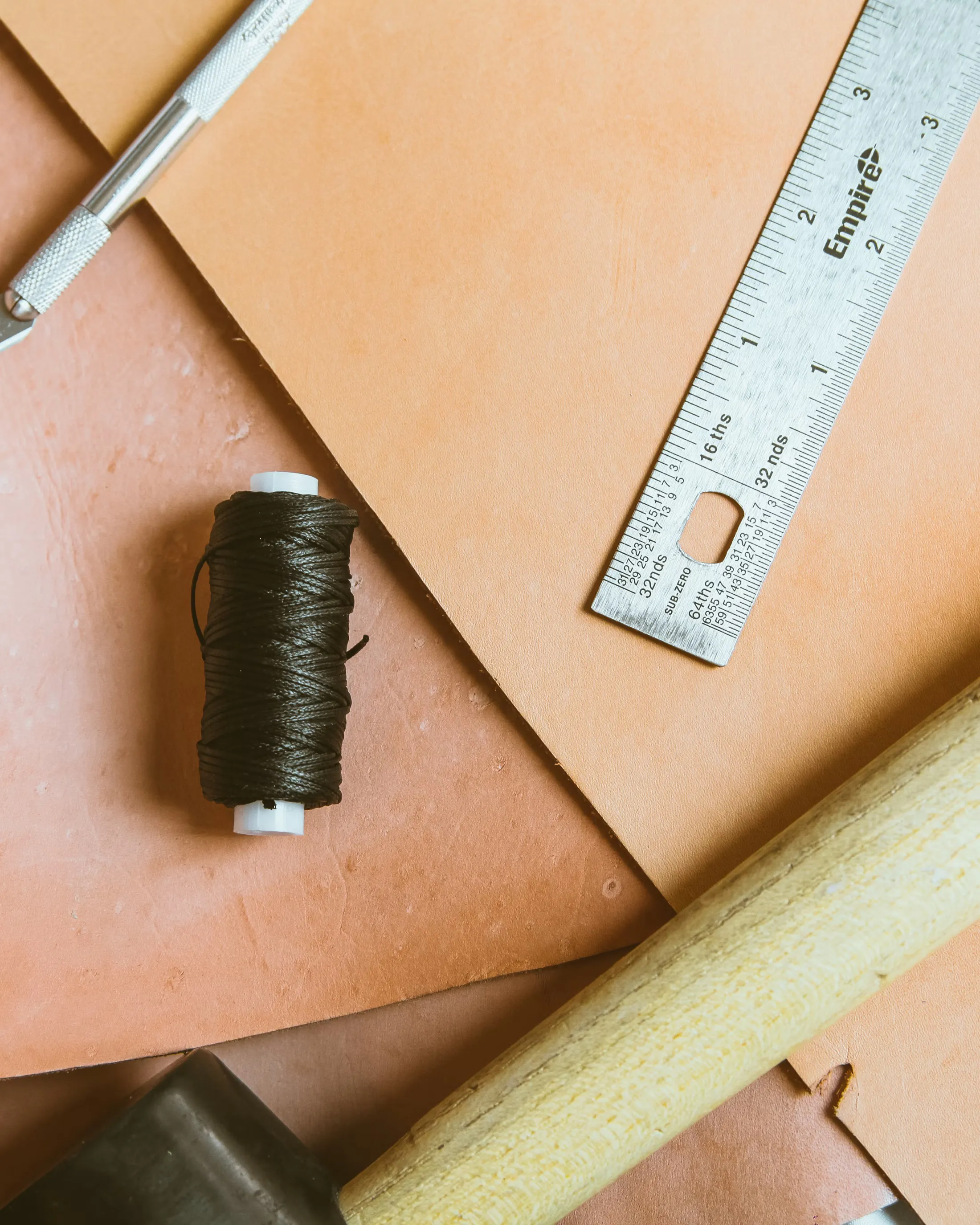 Leather cutting tools — hide, ruler, waxed thread, and knife on a workbench